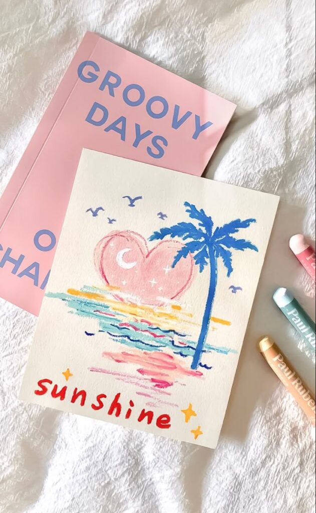 Colorful drawing of a heart-shaped sunset with palm tree and sunshine text, next to a pink Groovy Days notebook.