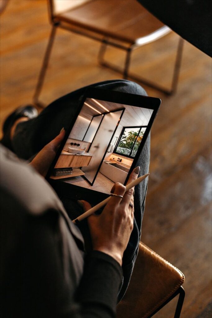 Person using digital tablet to view a modern bathroom design, with stylus in hand, in warm, ambient lighting.