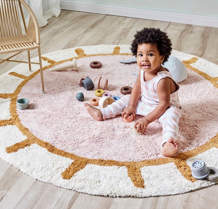 Smiling toddler playing with toys on a sun-themed rug in a cozy room.