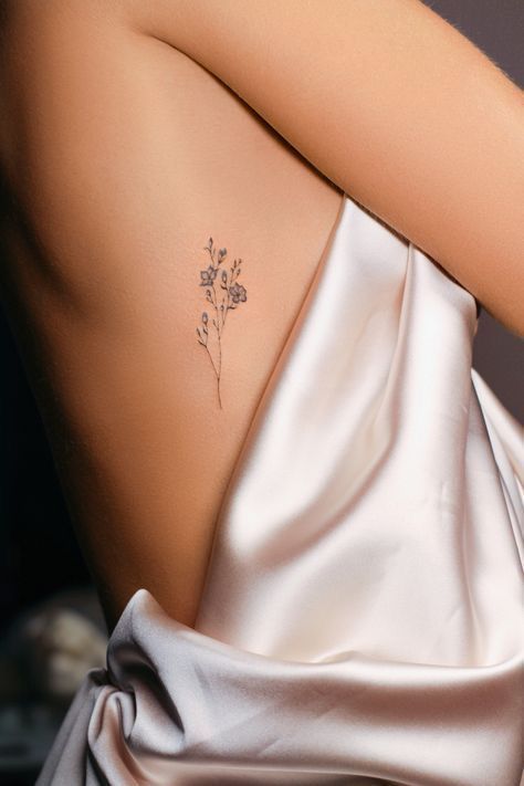 Minimalist flower tattoo on side of torso with smooth silk drape.