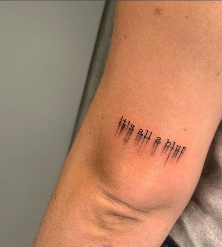 Arm tattoo reading it's all a blur with a smeared effect, located near the elbow.