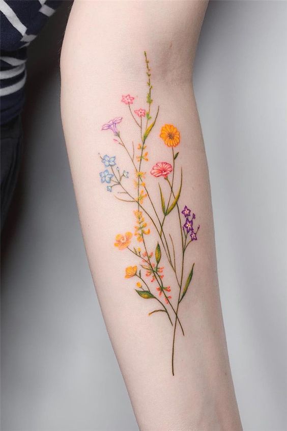 Delicate floral tattoo on forearm featuring colorful wildflowers in fine detail against a light skin tone.