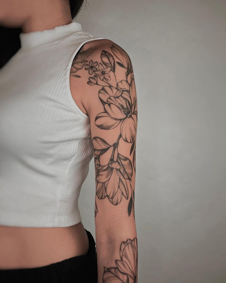 Black and white floral tattoo sleeve on woman's arm, wearing a sleeveless white top.