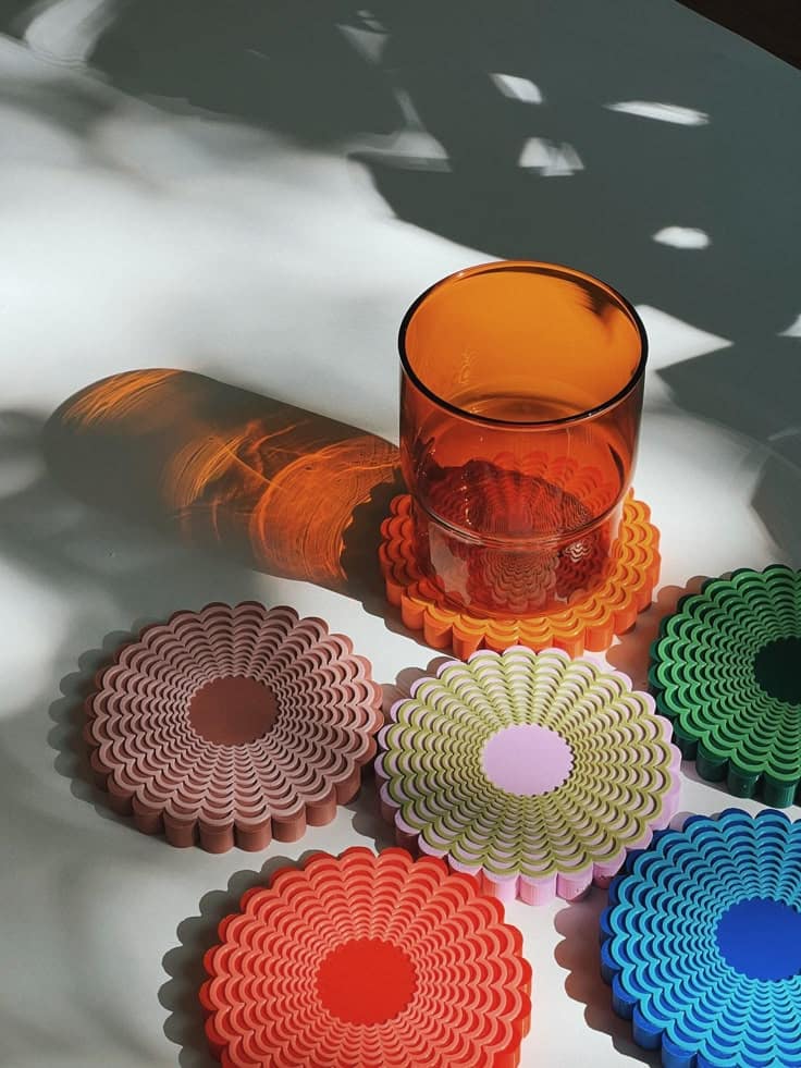 Colorful coasters with a vibrant orange glass, casting artistic shadows on a white surface.