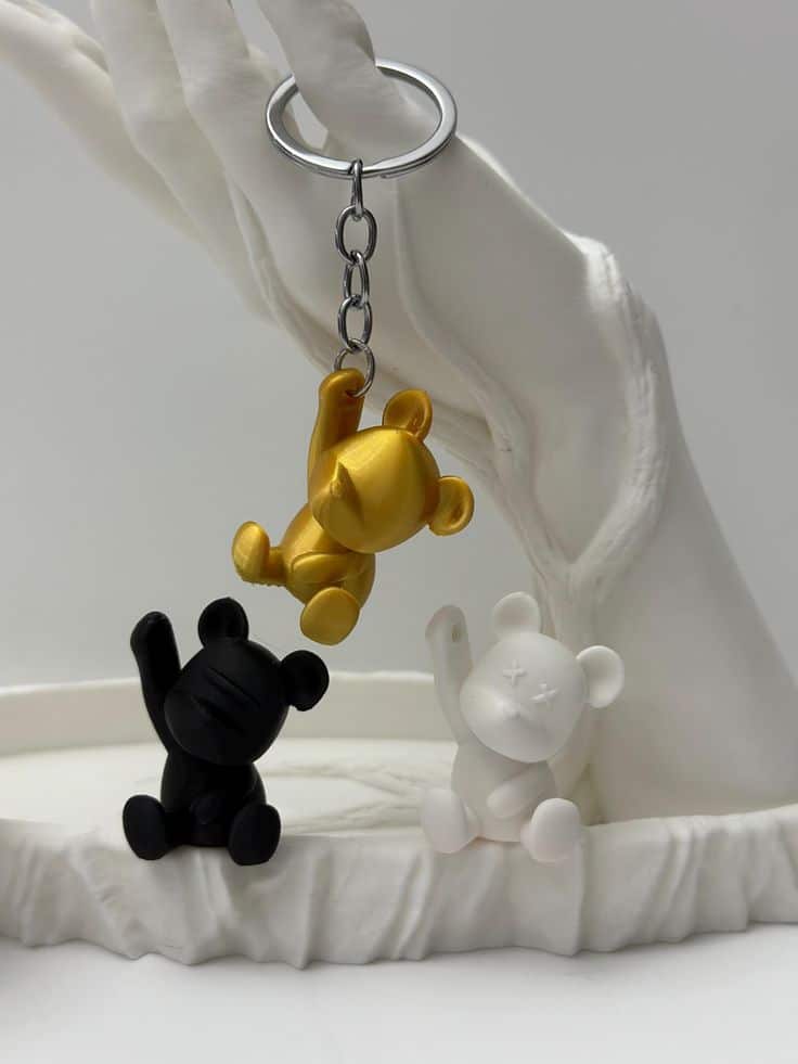 Keychain with gold, black, and white bear charms hanging from a decorative hand display.
