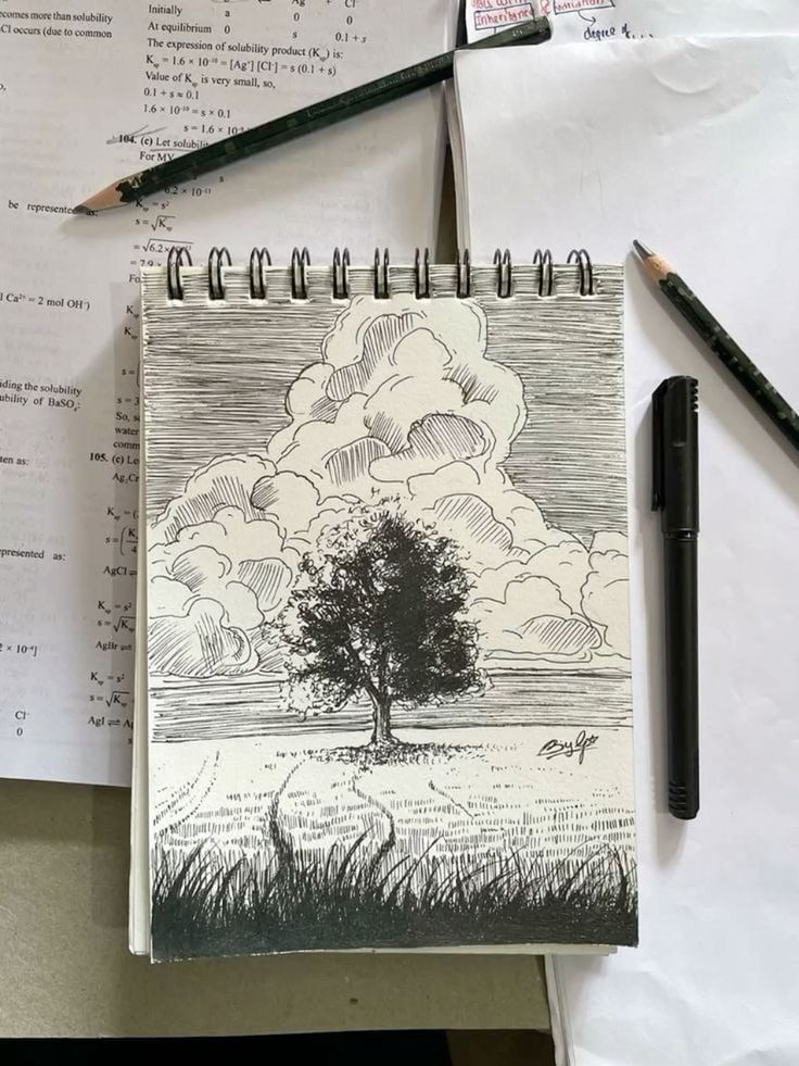 Sketch of a tree on a notebook surrounded by pencils and papers, showcasing creativity and artistic expression.