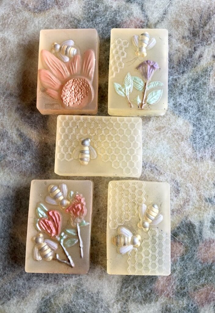 Handcrafted decorative soaps with bee and floral designs, showcasing intricate patterns and pastel colors.
