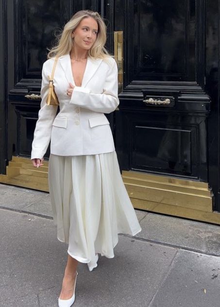 Woman in a stylish white blazer and dress, walking confidently past an elegant black door.