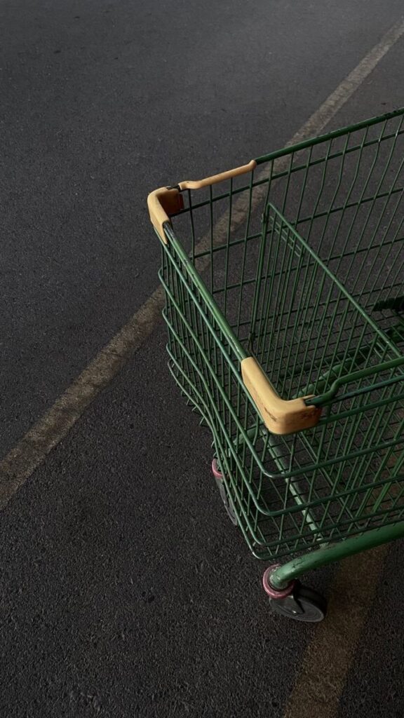 Green shopping cart on dark pavement, captured at an angle.