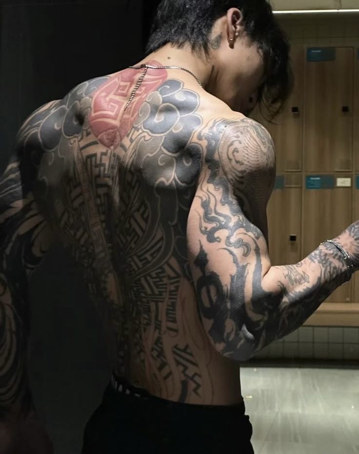 Person with detailed back and arm tattoos in a locker room setting, showcasing body art and muscle definition.