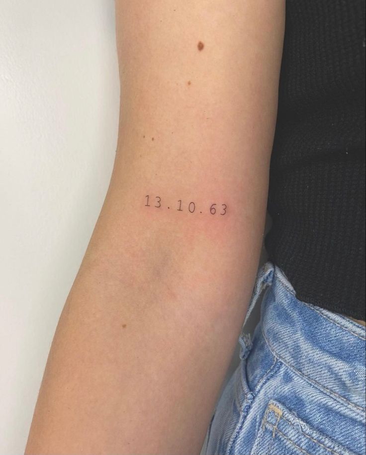 Minimalist arm tattoo displaying the date 13.10.63 in black ink, against a light skin background.