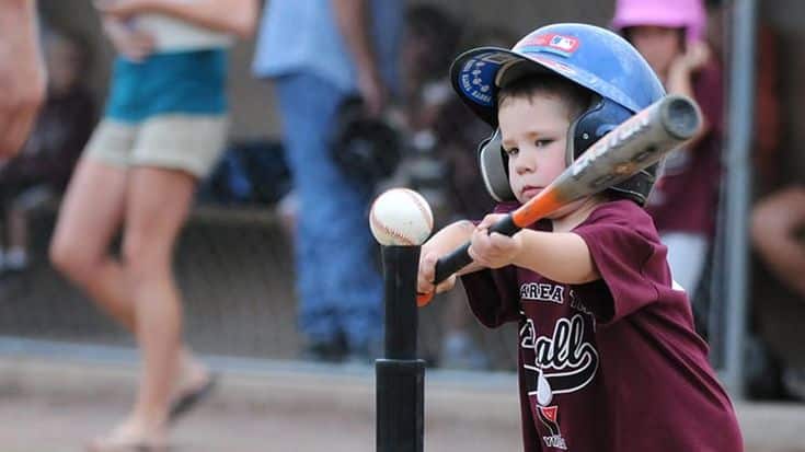 Young child in a helmet practicing tee-ball swing, focused on hitting the ball indoors.