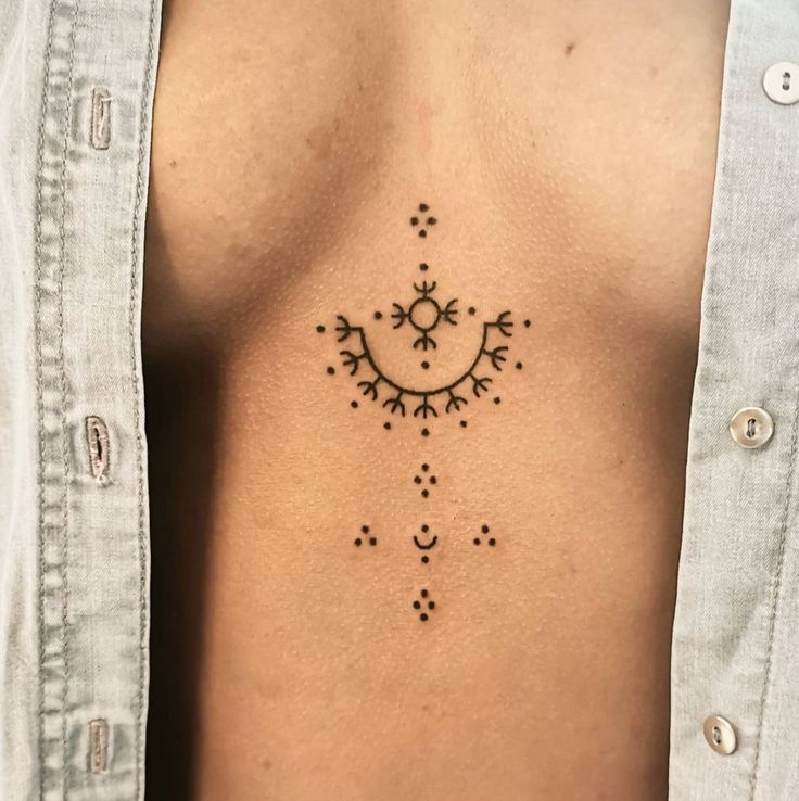 Close-up of minimalist geometric chest tattoo under an open shirt, featuring intricate dots and lines design.