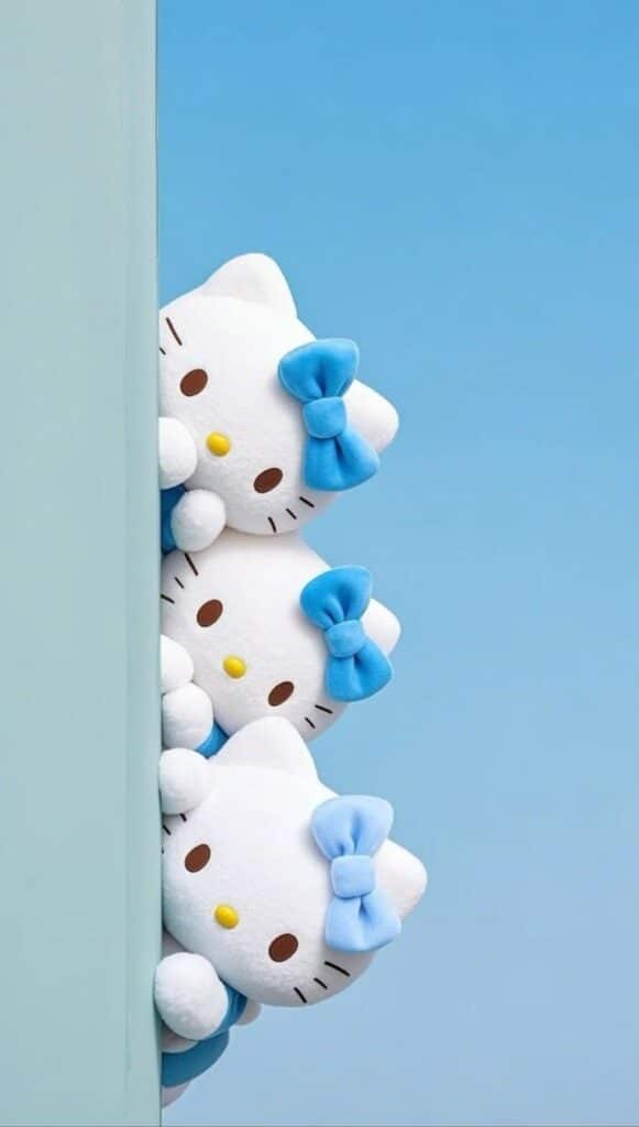 Three Hello Kitty plush toys with blue bows peek around a corner against a blue sky background.