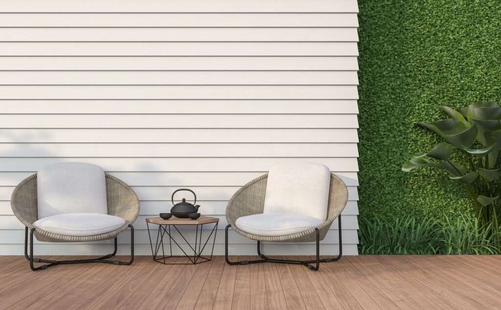 4054210-G10-1 Outdoor patio with two modern wicker chairs, table, and teapot against white siding and green foliage backdrop. | Sky Rye Design Outdoor patio with two modern wicker chairs, table, and teapot against white siding and green foliage backdrop.