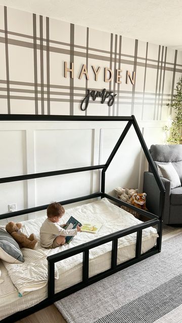 Toddler reading on a house-shaped bed in a cozy room with plaid wall design and neutral decor.