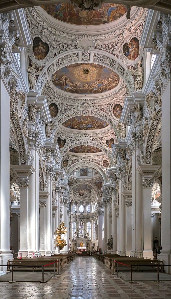 Ornate baroque church interior with frescoed ceilings, detailed columns, and a central aisle leading to the altar.