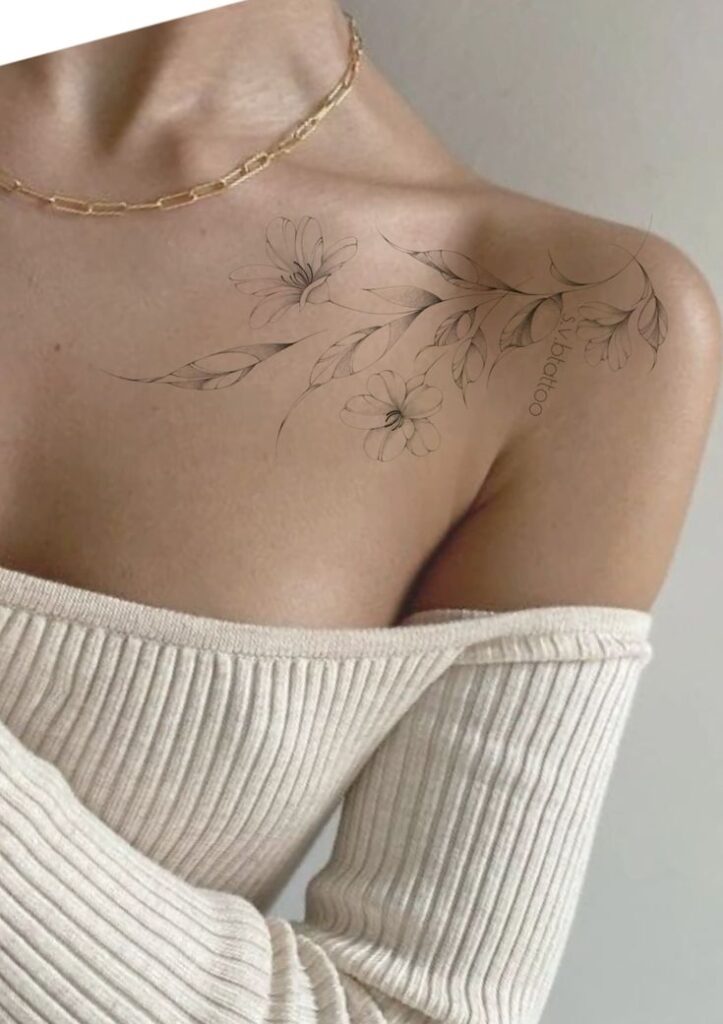 Elegant floral tattoo on woman's shoulder, wearing an off-shoulder ivory sweater, delicate and stylish.