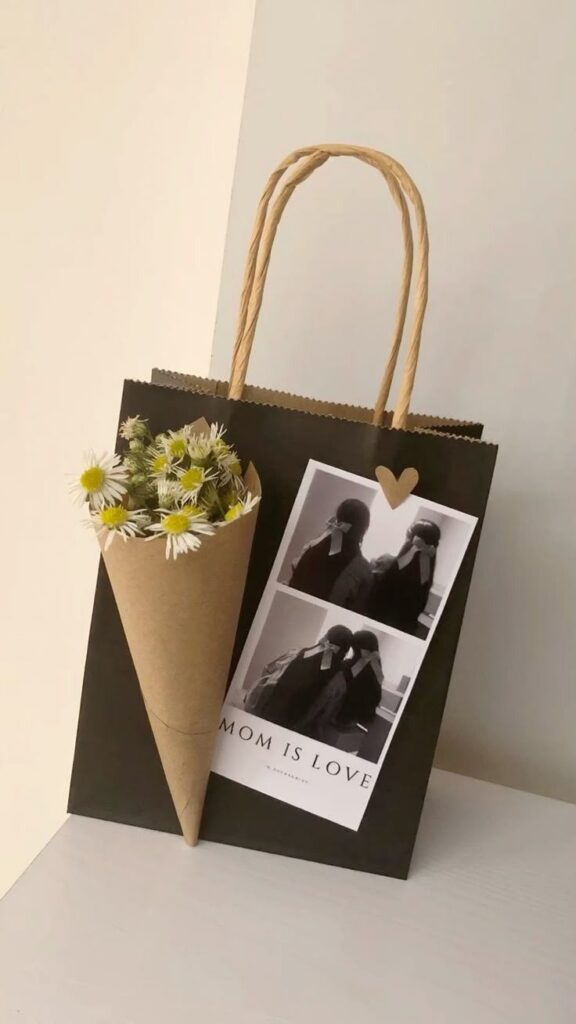 Gift bag with daisies and Mom is Love photo card on a white surface.