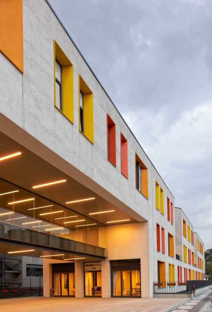_ 44 Modern building with colorful windows and glass entrance under a cloudy sky. | Sky Rye Design Modern building with colorful windows and glass entrance under a cloudy sky.