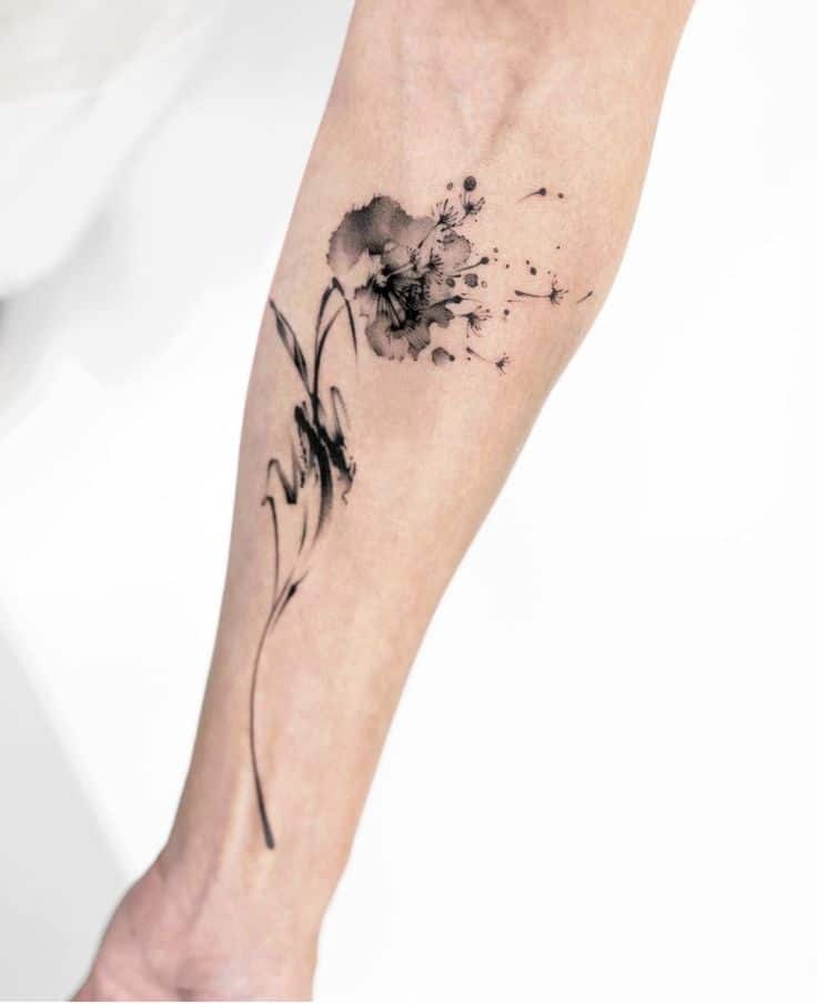 Abstract ink tattoo on forearm, featuring floral and splash elements in black.