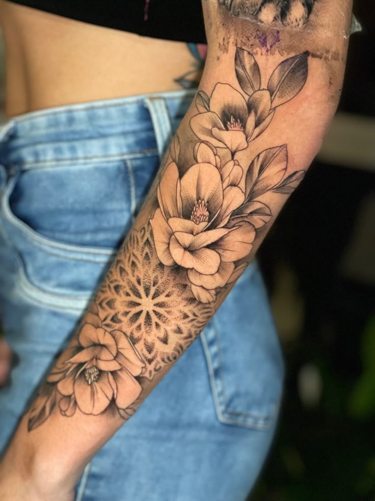 Floral arm tattoo with intricate black and gray patterns, showcasing blooming flowers and geometric designs.