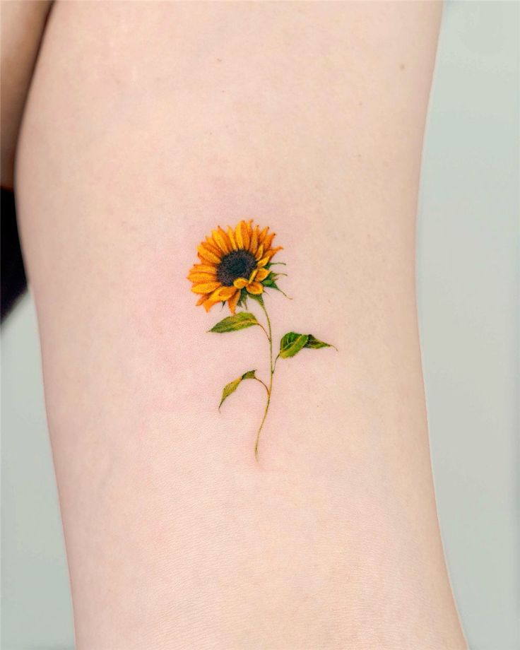 Sunflower tattoo on skin, showcasing a detailed and vibrant design with green leaves and a tall stem.