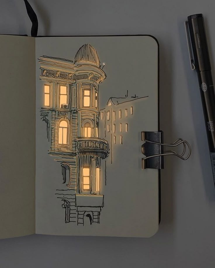Sketch of an illuminated building on a notebook page with a pen and clip.
