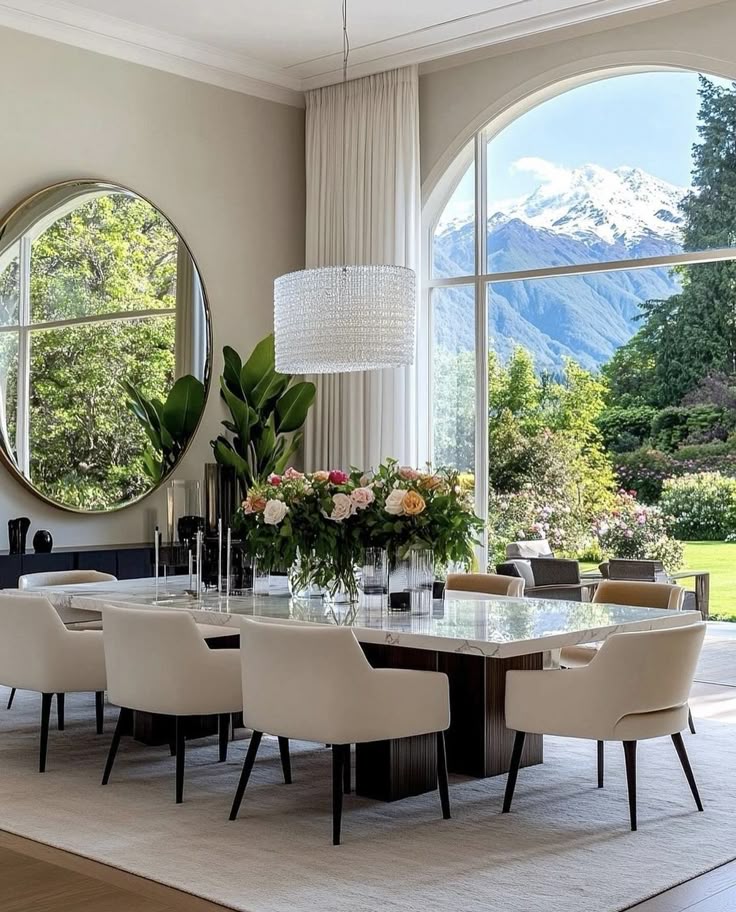 Elegant dining room with mountain view, featuring white chairs, floral centerpiece, and large mirror.