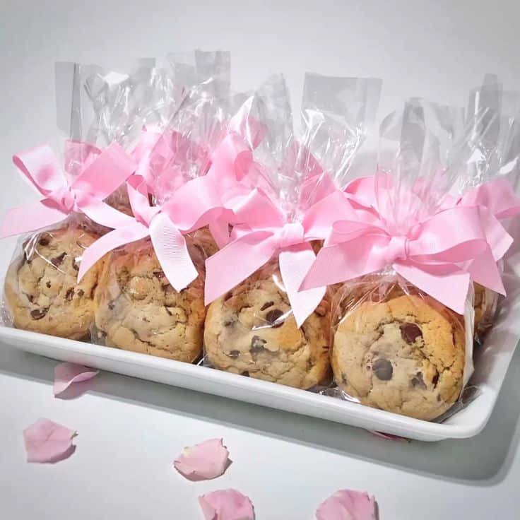 Gourmet chocolate chip cookies wrapped in clear bags with pink bows on a tray, perfect for gifts.