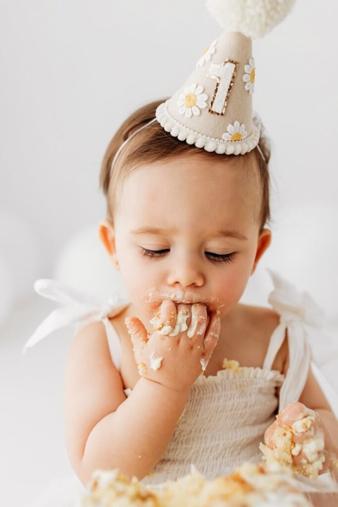Baby celebrating first birthday with cake, wearing a party hat.