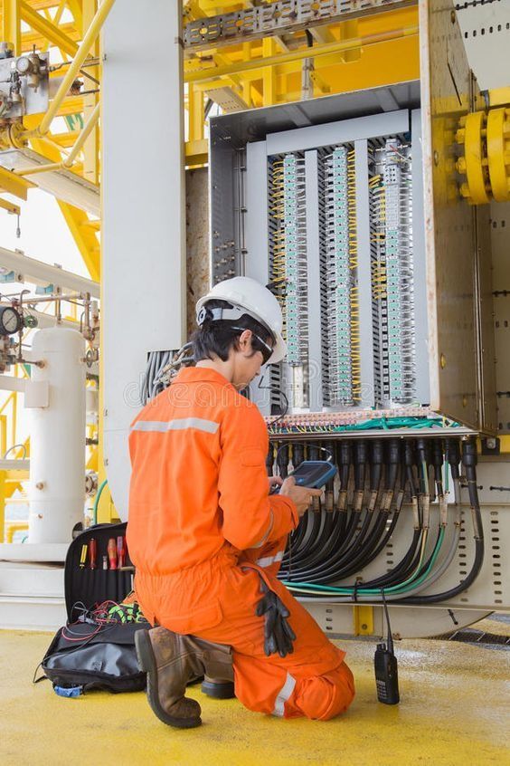 Technician in safety gear inspecting electrical panel in industrial setting.