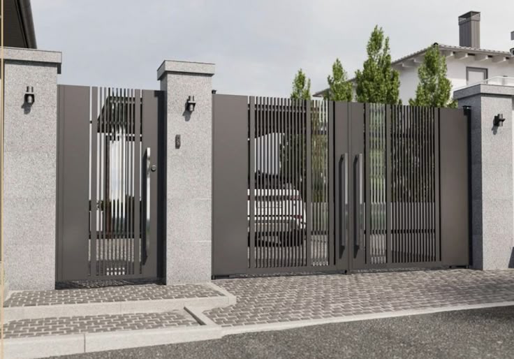 Modern gray metal gate with vertical bars, set in a stone wall, with a driveway and trees in the background.