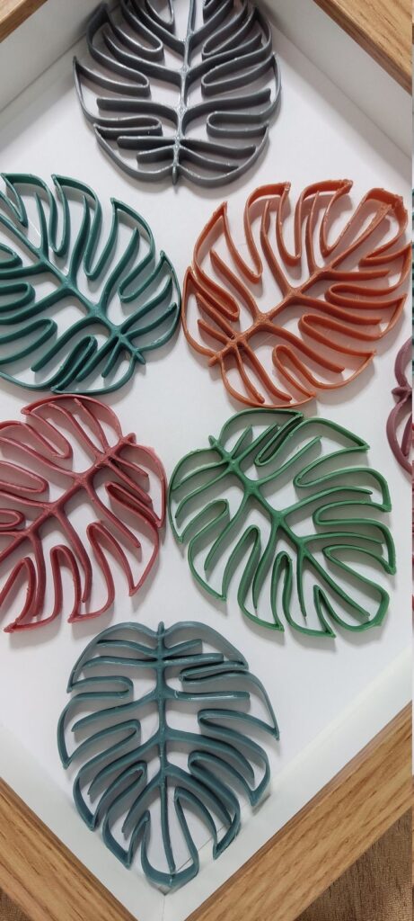 Colorful monstera leaf coasters in hexagonal wooden tray, arranged aesthetically on a white background.