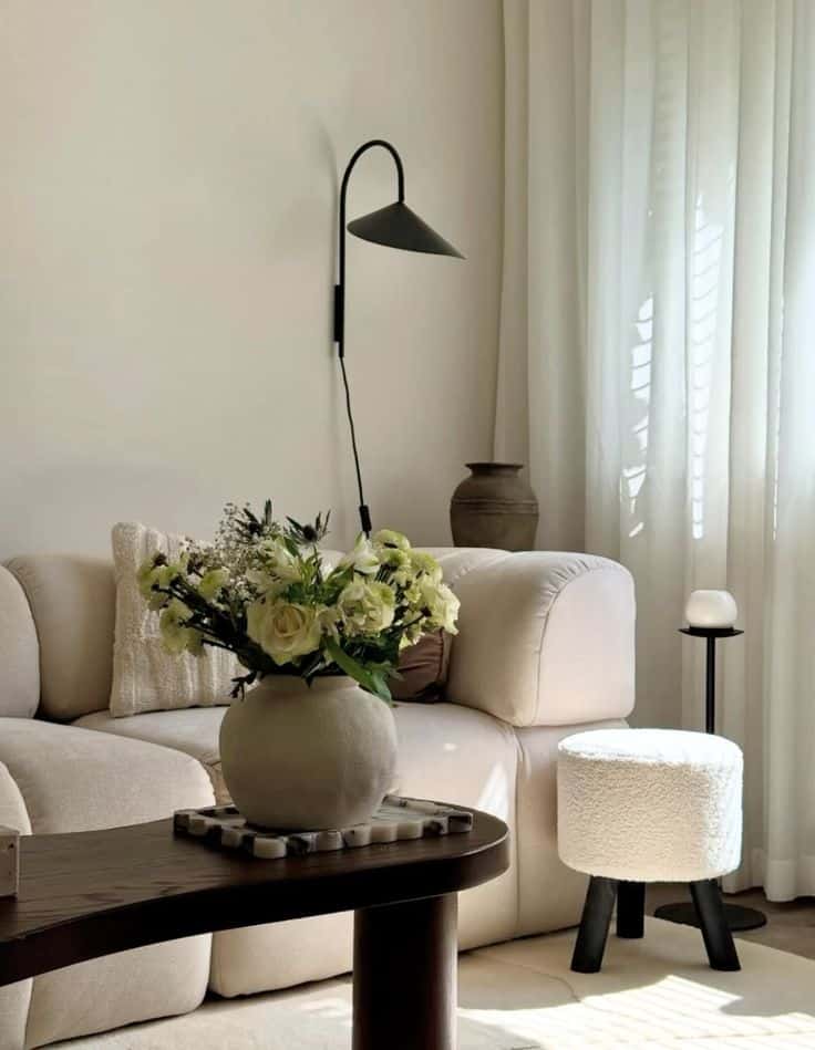 Modern living room with beige sofa, floral vase, and cozy decor in natural light.