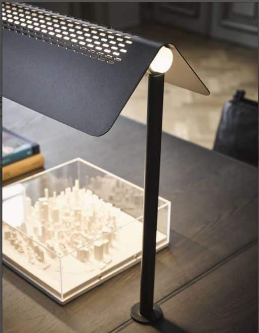 Modern desk lamp illuminating a detailed architectural model on a wooden table.