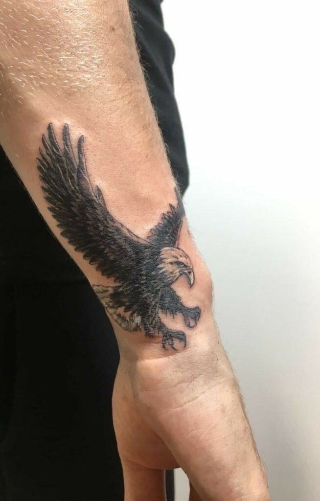 Eagle tattoo on forearm, wings spread, detailed black ink design on pale skin.