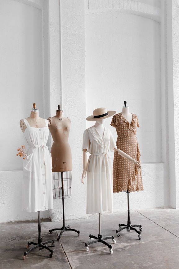 Four mannequins displaying elegant summer dresses in a minimalist setting with white and beige tones.