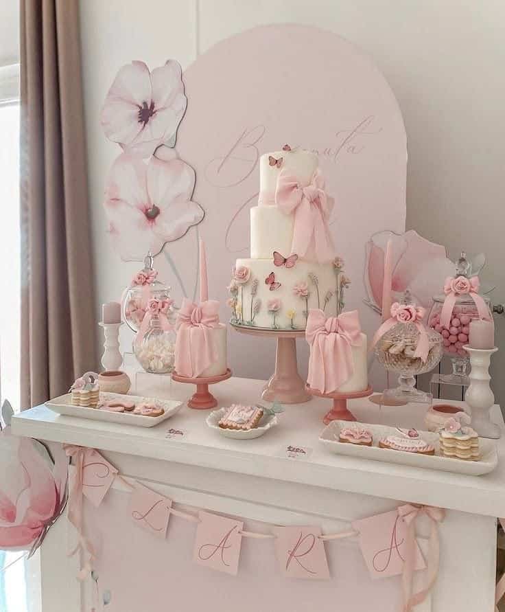 Elegant pink floral birthday dessert table with cake, sweets, and butterfly decorations. Perfect for a girly celebration.