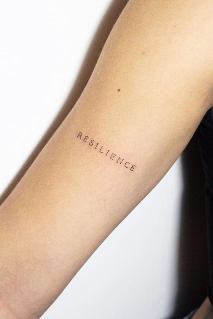 Tattoo of the word resilience on a forearm, emphasizing strength and perseverance in minimalist style.