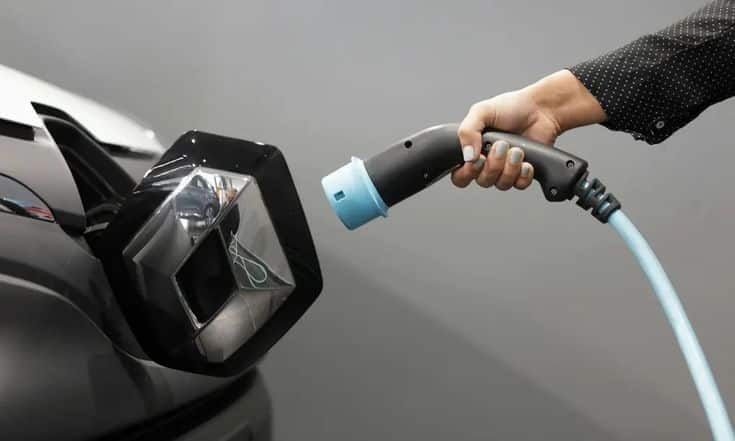 Hand plugging electric car into charging port, showcasing clean energy and sustainable technology.
