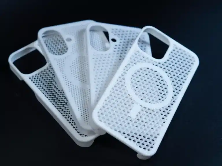 51f91878-f006-4c34-bf8e-cb48b01be83d White mesh smartphone cases stacked on a dark surface, featuring geometric cutout patterns. | Sky Rye Design White mesh smartphone cases stacked on a dark surface, featuring geometric cutout patterns.