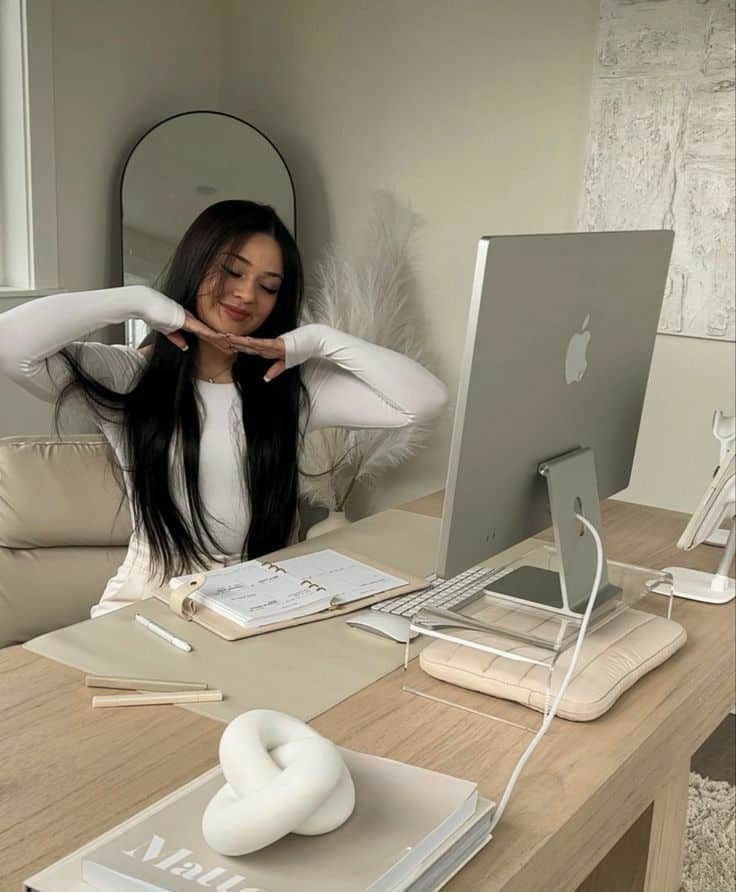 Woman smiling at desk with computer, planner, and modern decor in a bright home office setting.