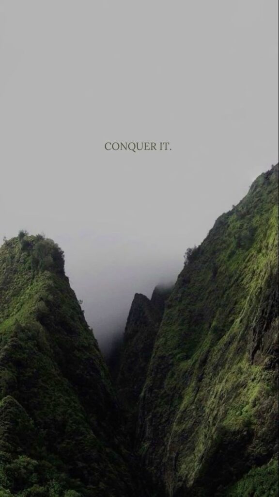 Mystical green cliffs shrouded in fog with motivational text Conquer It above. Perfect for inspiration and adventure themes.