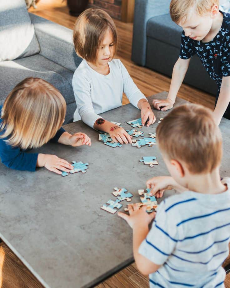 Children collaborating on a jigsaw puzzle on a table in a cozy living room.