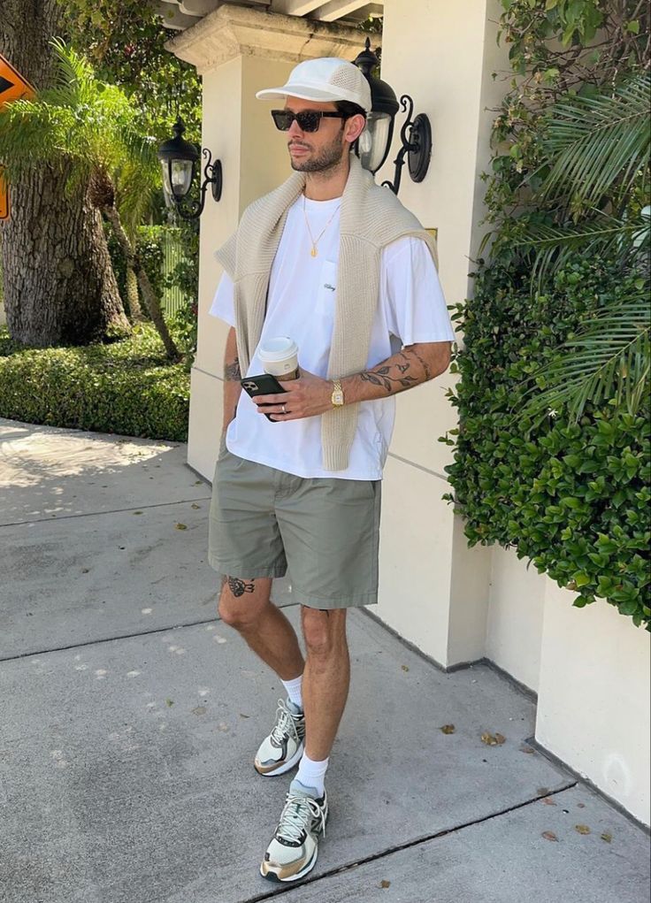 _ 6 Man in casual summer outfit with sunglasses, holding coffee and phone, outdoors with greenery background. | Sky Rye Design Man in casual summer outfit with sunglasses, holding coffee and phone, outdoors with greenery background.