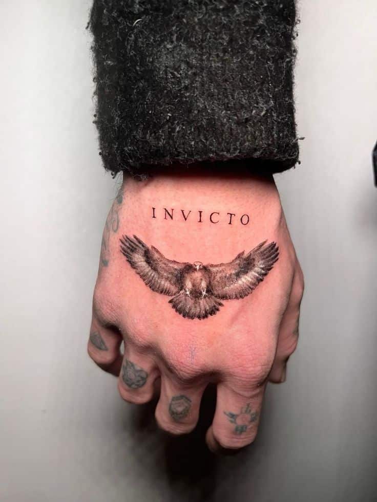 Hand tattoo with the word Invicto and an eagle design, showcasing intricate detail and bold ink work.
