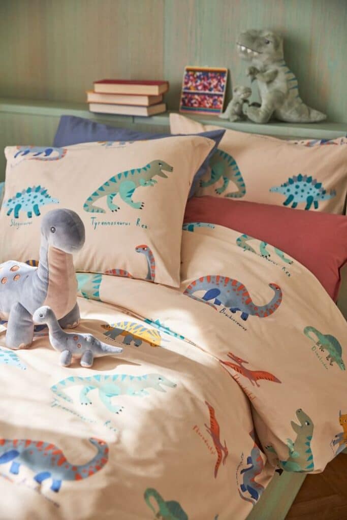 Colorful dinosaur-themed bedding and plush toys in a cozy kids' room.