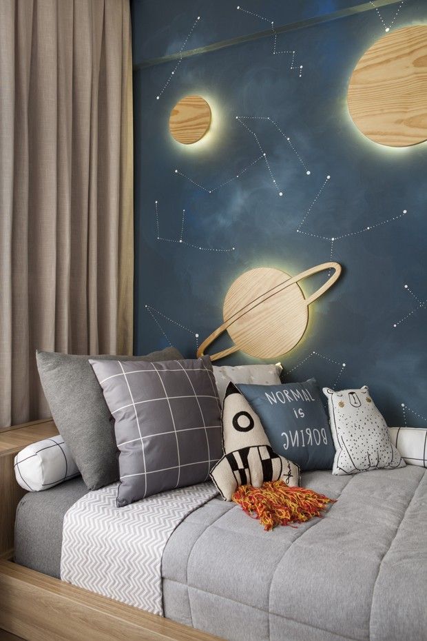 Kids' bedroom with space-themed decor, featuring planets, stars, and rocket pillows on a cozy bed.