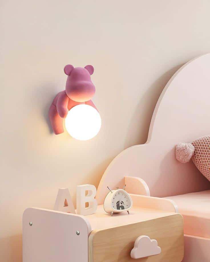 Cute kids' room with a pink hippo wall light and pastel decor, featuring ABC blocks and an alarm clock on a bedside table.